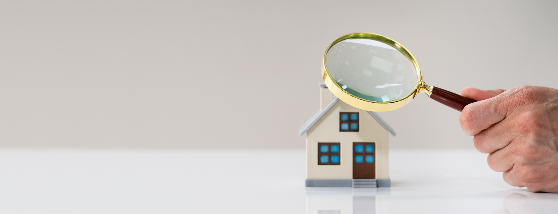 Image of an individual in a gray long sleeve shirt holding a magnifying glass over a small model home, meant to symbolize the revaluation process.