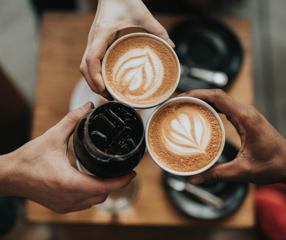 Image of three hands of different races holding up cups of coffee.