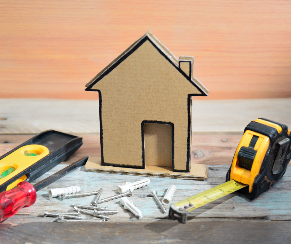 Image of a cardboard home cutout next to home repair tools.