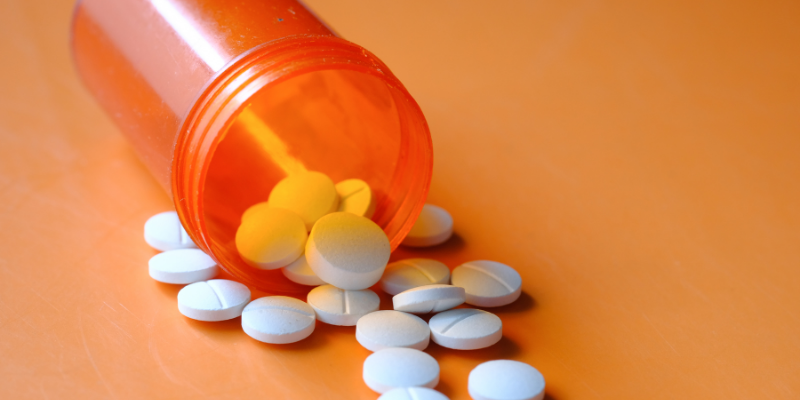 Image of an orange prescription bottle with white pills poured out onto an orange table.