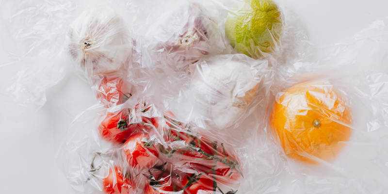 Image of a lime, an orange, onions, garlic, and tomatoes in transparent plastic bags.