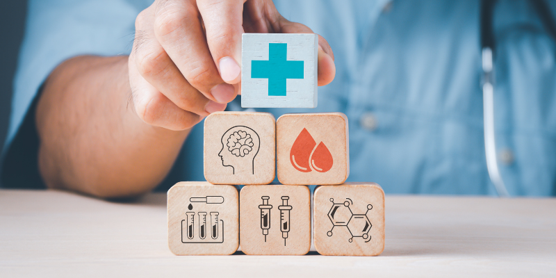 Image of a white individual in a pale blue shirt stacking several tabletop wooden blocks adorned with healthcare motifs.