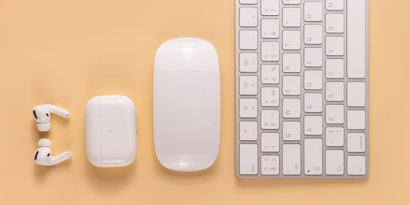 Image of white ear buds, headphone case, mouse, and keyboard aligned in order from smallest to largest on a peach background.