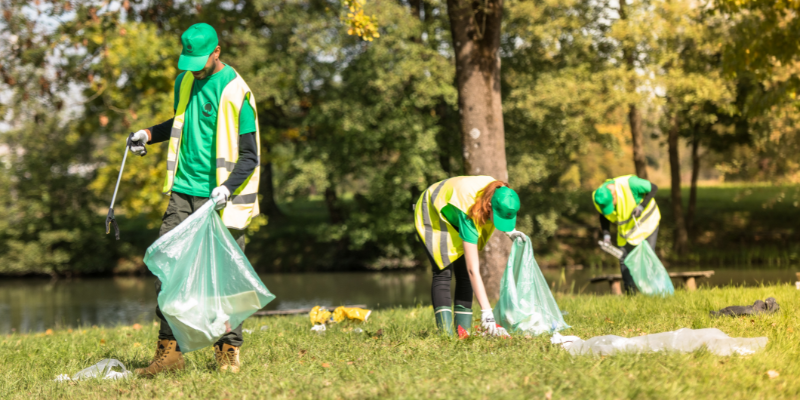 Image of three individuals of different races and gender expressions picking up litter in an outdoor community space.