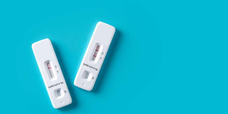 Image of two COVID rapid tests, one with a positive result and one with a negative result, on a blue background.